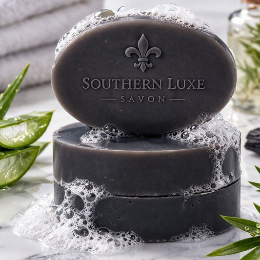 Black soap bar with 'Southern Luxe Savon' branding on a marble surface with green leaves.